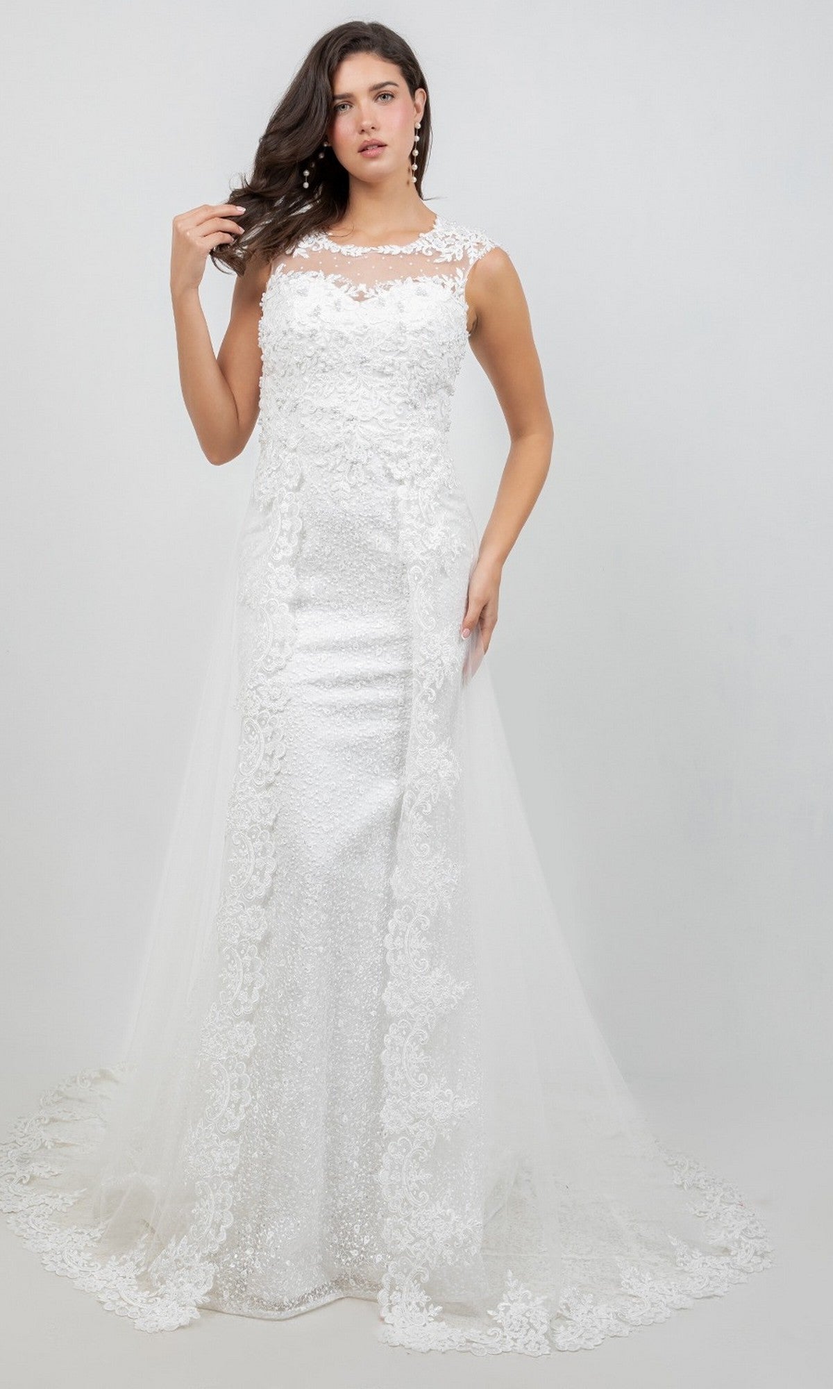 A woman wearing the Cinderella Couture 8506J, a long formal white sleeveless lace wedding dress featuring elegant lace appliques and a dramatic train, stands against a plain light background.
